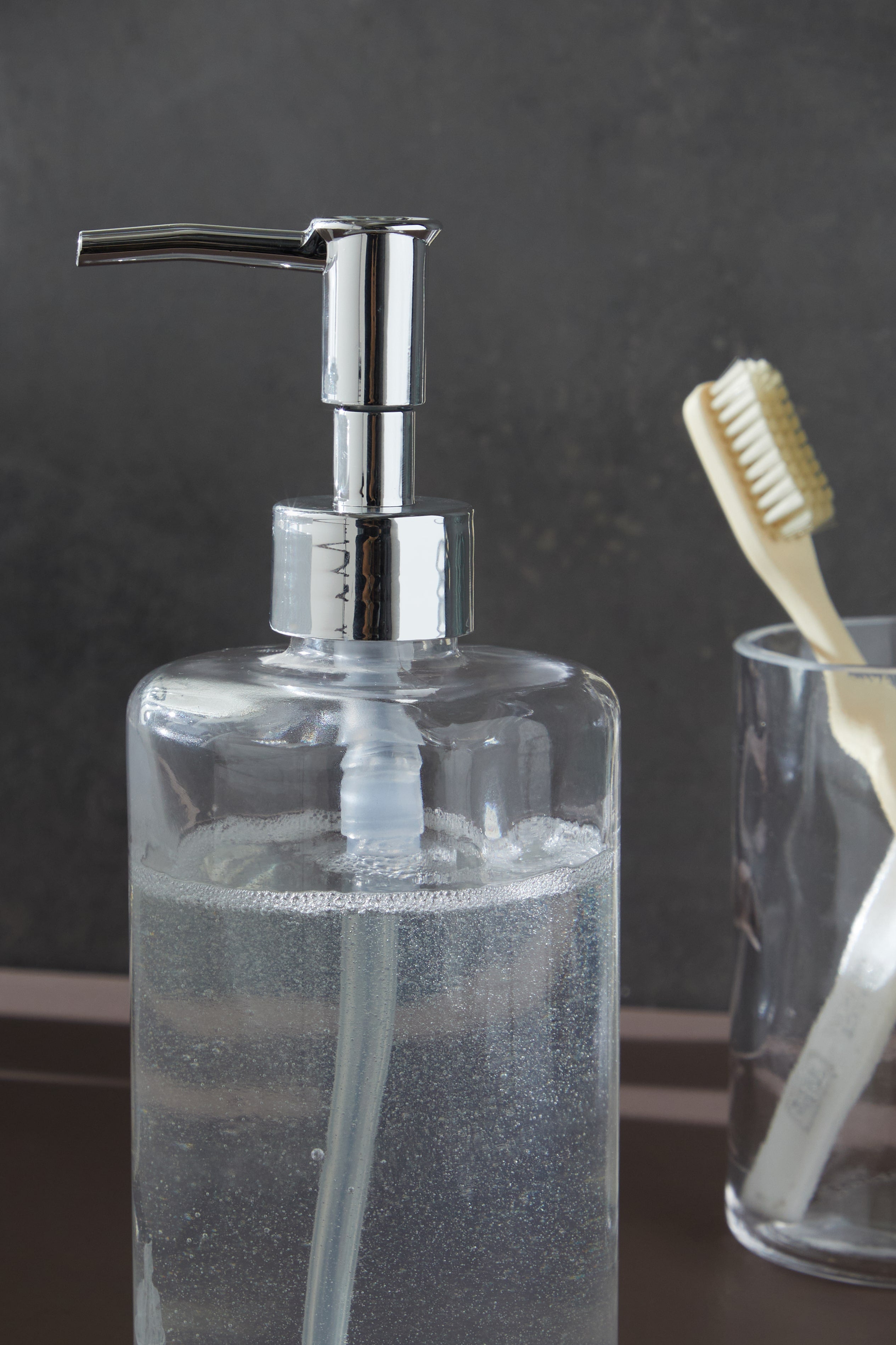 Glamis Clean Model Banyo Takımı 3'lü Set - Modern tasarımlı sıvı sabunluk, şıklık ve lüks ile banyonuzda zarif bir görünüm sunuyor. Arka planda diş fırçası ve diş fırçalık ile tamamlanmış bir banyo düzeni.