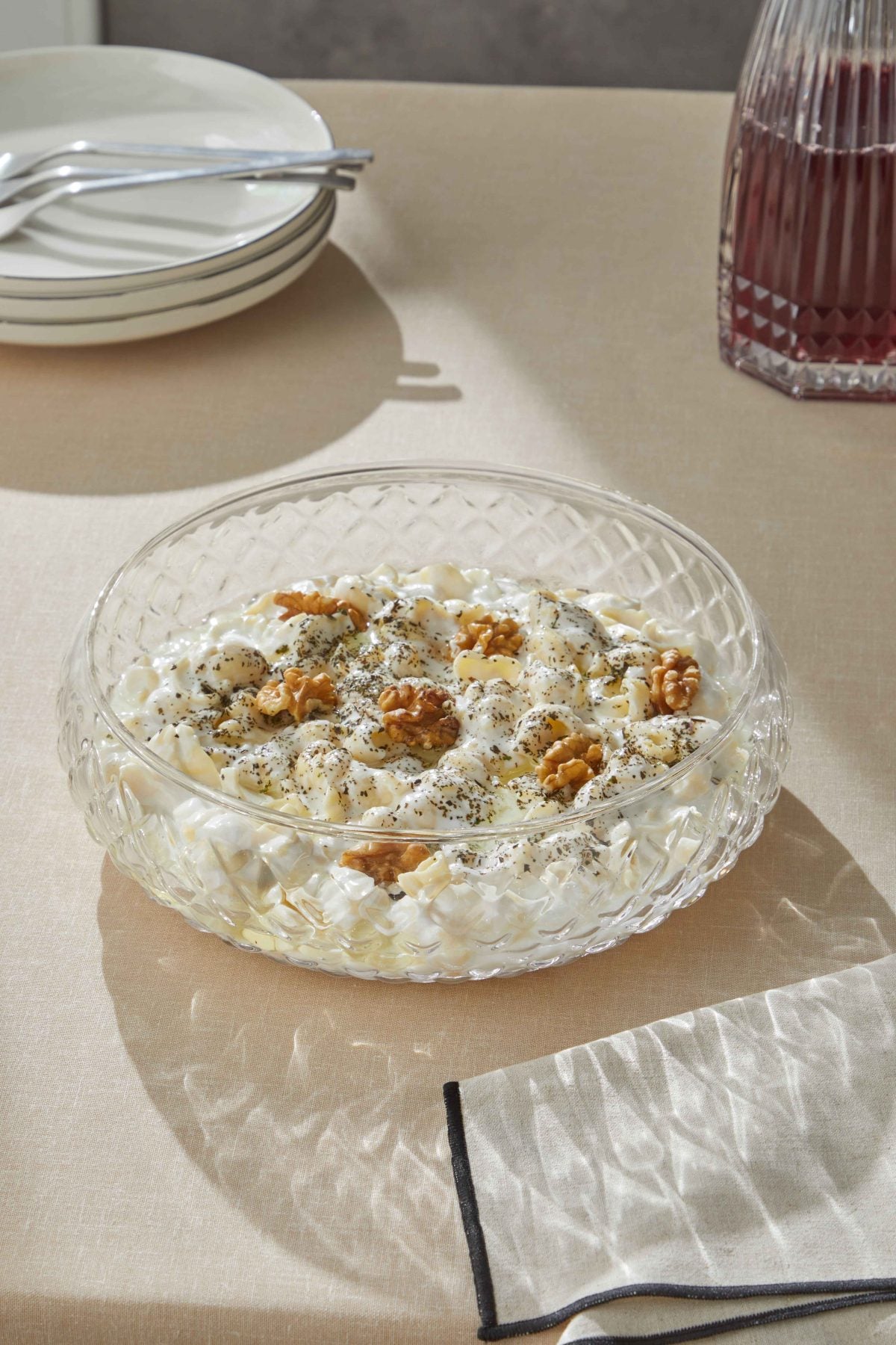 Glamis Kafes Model Büyük Boy Cam Salata Kasesi, üstünde ceviz ve baharatlarla hazırlanan salata ile birlikte, estetik bir masa örtüsü üzerinde sunuluyor. Şık ve modern tasarımıyla göz alıcı.